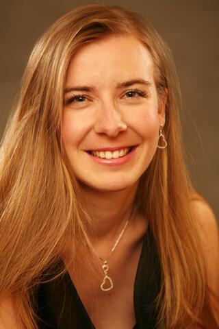 Photograph of Veronika Pikola Brazdilova. Woman with blonde hair. Wears gold necklace with heart shaped pendant. Wears gold earings with heart shape.