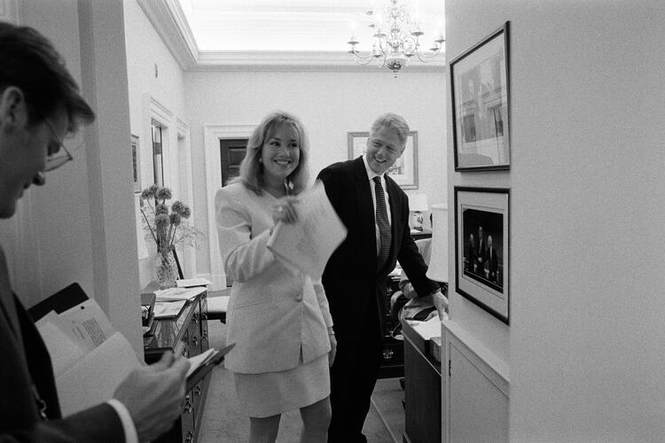 President Clinton laughs with Director of the Office of Scheduling and Advance, Stephanie Streett, and President's Aide, Stephen Goodin in the hallway outside of the White House Oval Office.  President Clinton, Street and Goodin all stand in the hallway. Goodin looks down at documents. 