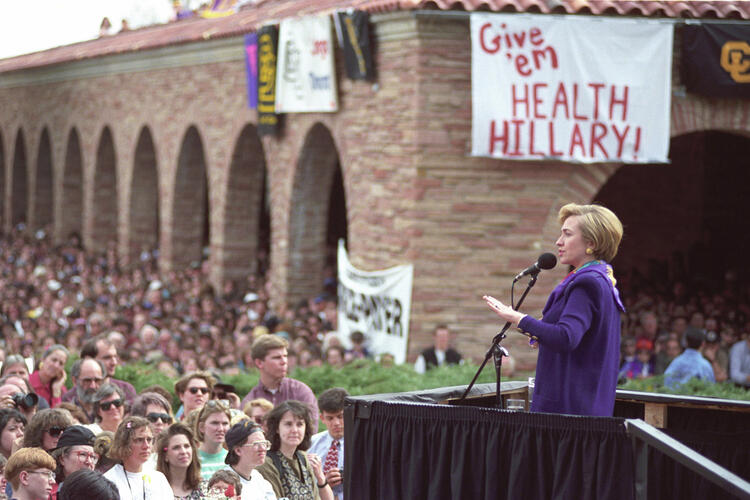 First Lady Hillary Rodham Clinton addressing a health care rally at the University of Colorado at Boulder, a sign in the background reads "Give em' Health Hillary!"