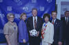In the center, President Clinton holds the Questra, the official match ball of the tournament. To his left, Hillary Clinton wears a blue checkered blazer, and to his right is Alan Rothenberg. Also present are two women: one on the far left wearing a tan blouse and an event credential, and another in a cream-colored blazer with a colorful scarf standing next to the President. They are all positioned in front of a blue step and repeat backdrop featuring the WorldCupUSA94 and FIFA logos.