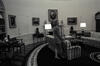 Oval Office Black and white photograph. First Lady Hillary Rodham Clinton standing alone next to a striped sofa in the Oval Office