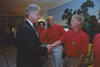President Bill Clinton shakes hands with a blonde US soccer player in a red team polo shirt inside the White House. The player previously shaking hands stands behind him, along with other teammates.