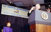President Clinton stands at a podium as he addresses New York City Wall Street Project event at the World Trade Center in New York, New York. Alexis Herman sits behind the President.