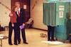 Voting in Cappaqua President Clinton hugs Chelsea Clinton outside of a aqua color voting booth. The booth's curtain is closed. Both are standing. President Clinton wears a suit.