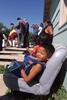 Event at Pine Ridge Reservation Oglala Sioux boy sits on a car bench outside his house. President Clinton can bee seen standing in the background.