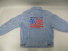 The back view of a light blue denim jacket features the official logo for the 1994 FIFA World Cup embroidered across the center. The embroidered design includes a blue soccer ball on the left, trailing three diagonal red stripes that merge into three horizontal red stripes, mimicking a waving flag. Above the graphic, the text "WorldCupUSA94" is stitched in black and red, underscored by a row of small blue dots. The jacket has visible seams, a pointed collar at the top, and two adjustment buttons on the bot