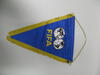 A triangular blue fabric pennant is displayed vertically against a plain light grey background, suspended by a thin gold chain attached to a horizontal metal rod at the top. The pennant features the word "FIFA" printed in solid yellow block letters across the center. Directly above the text, two overlapping soccer balls are illustrated, with the continents of a world map filled in black on their panels. The two sides of the triangle are trimmed with thick, golden-yellow fringe that tapels down to a point...