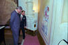 President Clinton and Václav Havel stand, looking down at a painting on the wall of Prague Castle. The painting is of a woman in a mask, holding a cat, and a clown leaning on a railing.