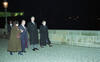 Photograph taken at night. President Clinton, President Vaclav Havel, Ambassador Madeleine Albright, President Clinton's Security Staff, and an unknown woman all wall across a stone bridge. They all wear overcoats. The lights of the city of Prague can be seen in the background.