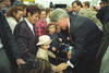 President Clinton leans over to speak with a little girl in a crowd. The girl wears a matching hat and coat. A woman stands behind the girl. 
