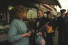First Lady Hillary Rodham Clinton stands holding a bouquet of flowers, speaking with Victoria "Violet" Clarke. Clarke holds a camera in her hands and wears a light blue sweater. Two uniformed policemen stand in the background.