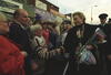 Hillary Rodham Clinton holds flowers and shakes hands with a women in a crowd of people.