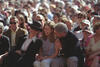 Convocation Ceremony at Stanford University President Clinton, First Lady Hillary Rodham Clinton, and Chelsea Clinton laughing. The sit outside in the front of a crowd of people. The first Lady wears a dark colored hat and dark sunglasses. Chelsea sits between Hillary and Bill Clinton