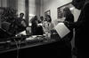 Black and white photo. President Clinton sits at a desk all the others in the room stand