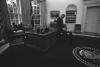 Black and white photograph. President Clinton sits on the edge of the Resolute Desk and plays with Buddy the Dog in the Oval Office following a briefing prior to a Radio Address