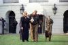 The President & First Lady walk to Marine One with Buddy the Dog. The Hillary Rodham Clinton Wears a long coat, scarf, and sunglasses. President Clinton looks down at buddy and wears a leather bomber jacket.