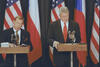 President Clinton and President Václav Havel stand behind podiums. President Havel wears erphone headset for translation. Bhind them are three United States flags and two Czech Republic flags.  