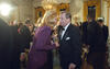 President Václav Havel holds a glass of sparkling wine in his hand and leans toward his wife, Dagmar Havlová. Havlová leans towards Havel and holds a glass of wine. Havel wears a tuxedo, and Havlová wears a violet/ or purple dress. 