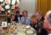 First Lady Hillary Rodham Clinton and President Václav Havel sit around a round table. Four other people sit also sit around the table. The table is set with stem wear and White House China. A large center piece of white and pink roses sits on the table