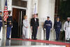 President Clinton and First Lady Hillary Rodham Clinton stand omn a red carpet in front of the White House. Six uniformed military personnel stand at attention. 