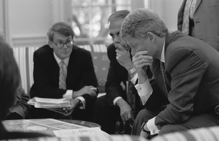 Black and white photograph. President Clinton participates in a scheduling meeting with Director of the Office of Scheduling and Advance, Billy Webster. President Clinton is shown with his hand covering his mouth in thought.