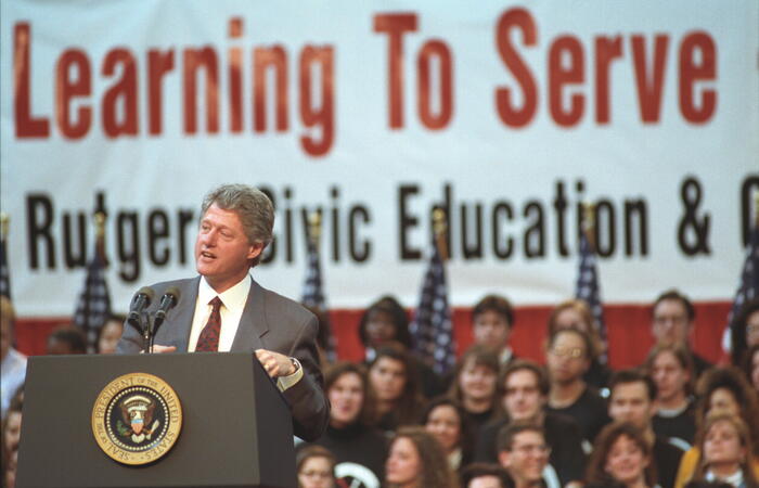 President Clinton delivers a National Service address to students in the gymnasium at Rutgers University. The backdrop reads "Learning to Serve - Serving to Learn Rutgers Civic Education & Community Program"