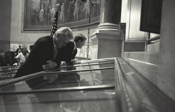 Black and white phtograph. President Clinton and Vice President Gore read the United States Constitution on display in the rotunda at the National Archives in Washington, D.C. prior to the President's speech on affirmative action.