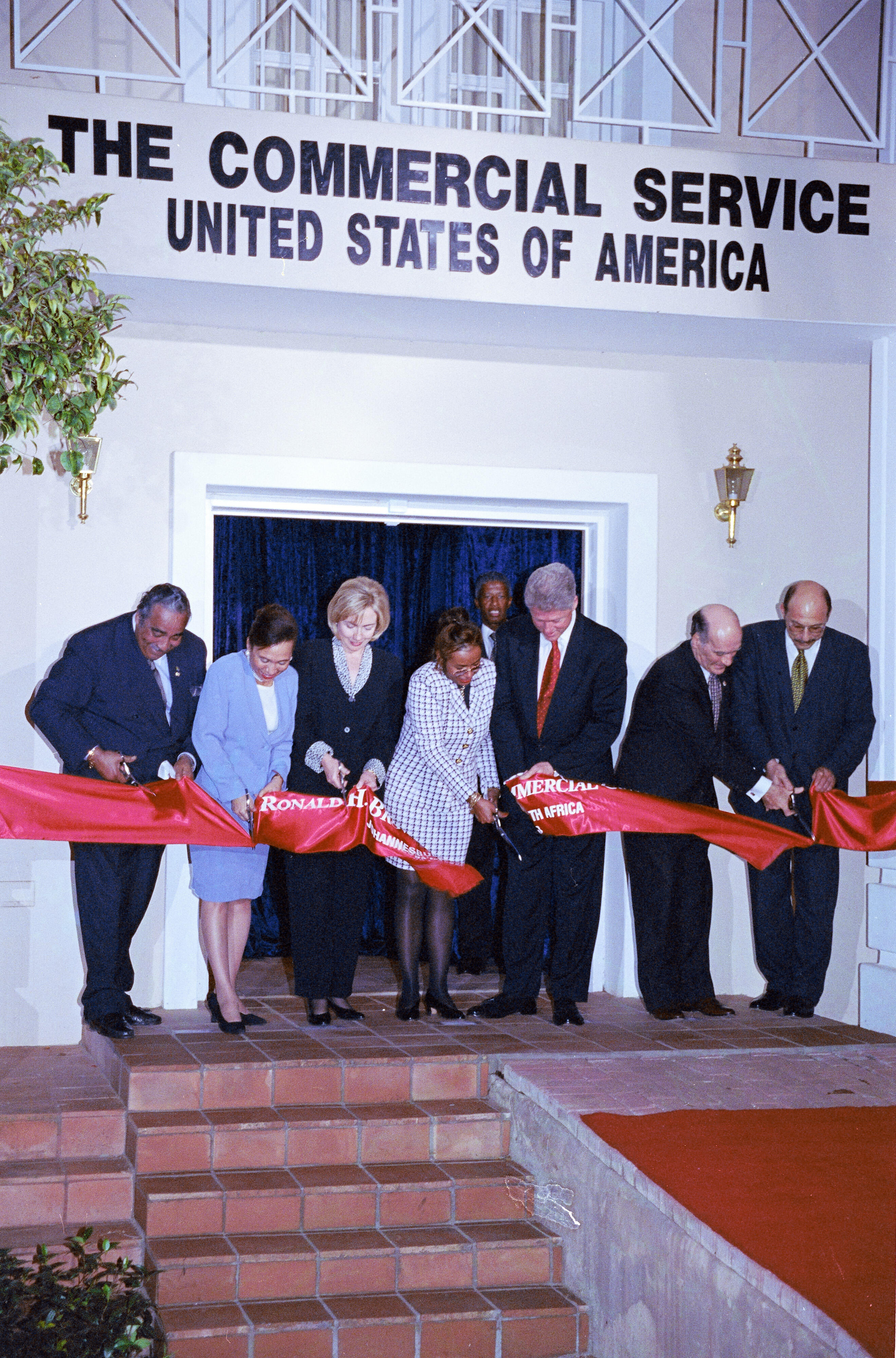 President Clinton, Hillary Rodham Clinton, Alma Brown, Alexis Herman, Charles Rangel, lean over to cut a ribbon in front of the Ronald H. Brown Commercial Center.