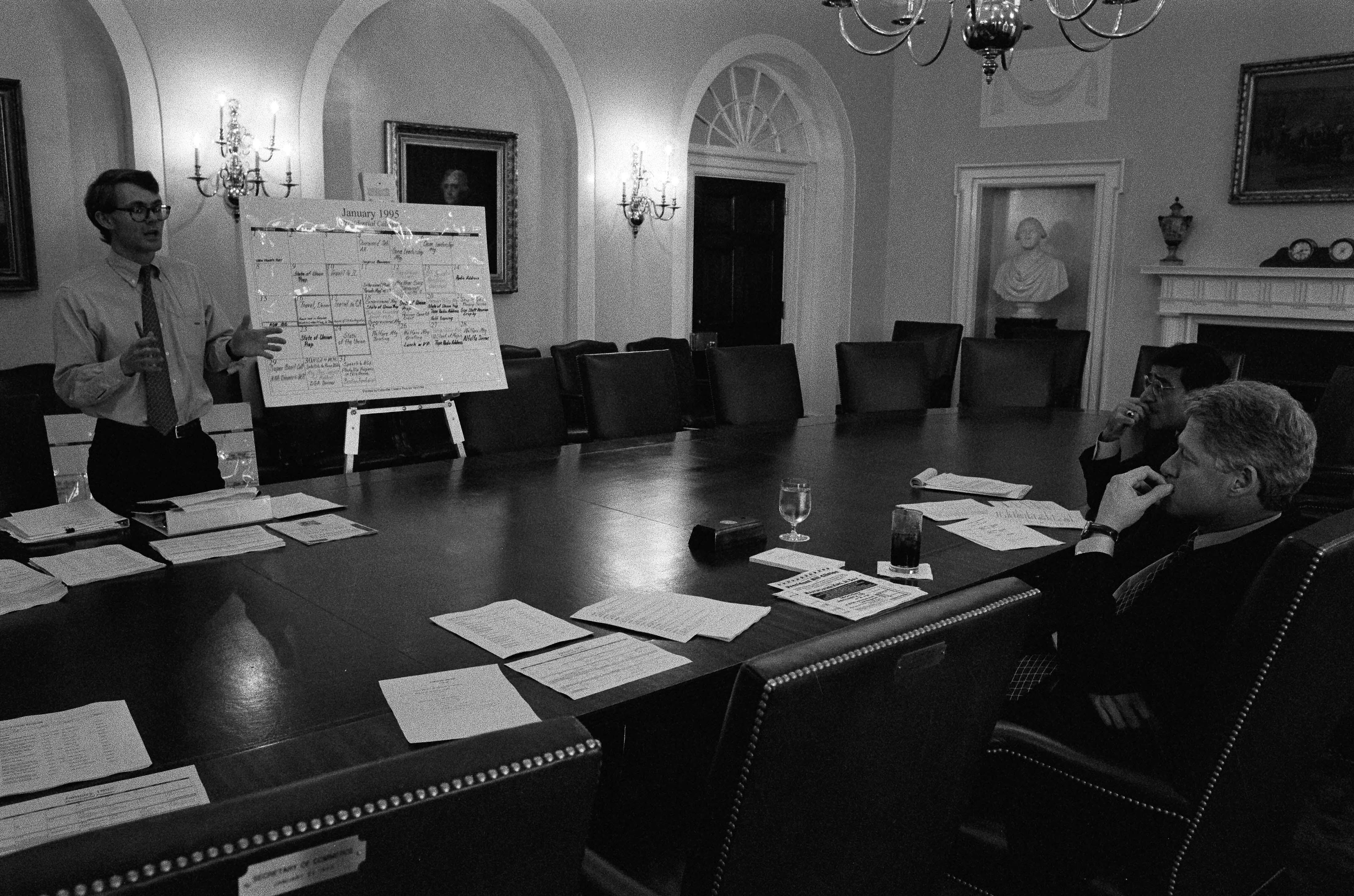 President Clinton participates in a scheduling meeting with Director of the Office of Scheduling and Advance, Billy Webster. President Clinton sits in the Cabinet room. Webster stands next to a chart.