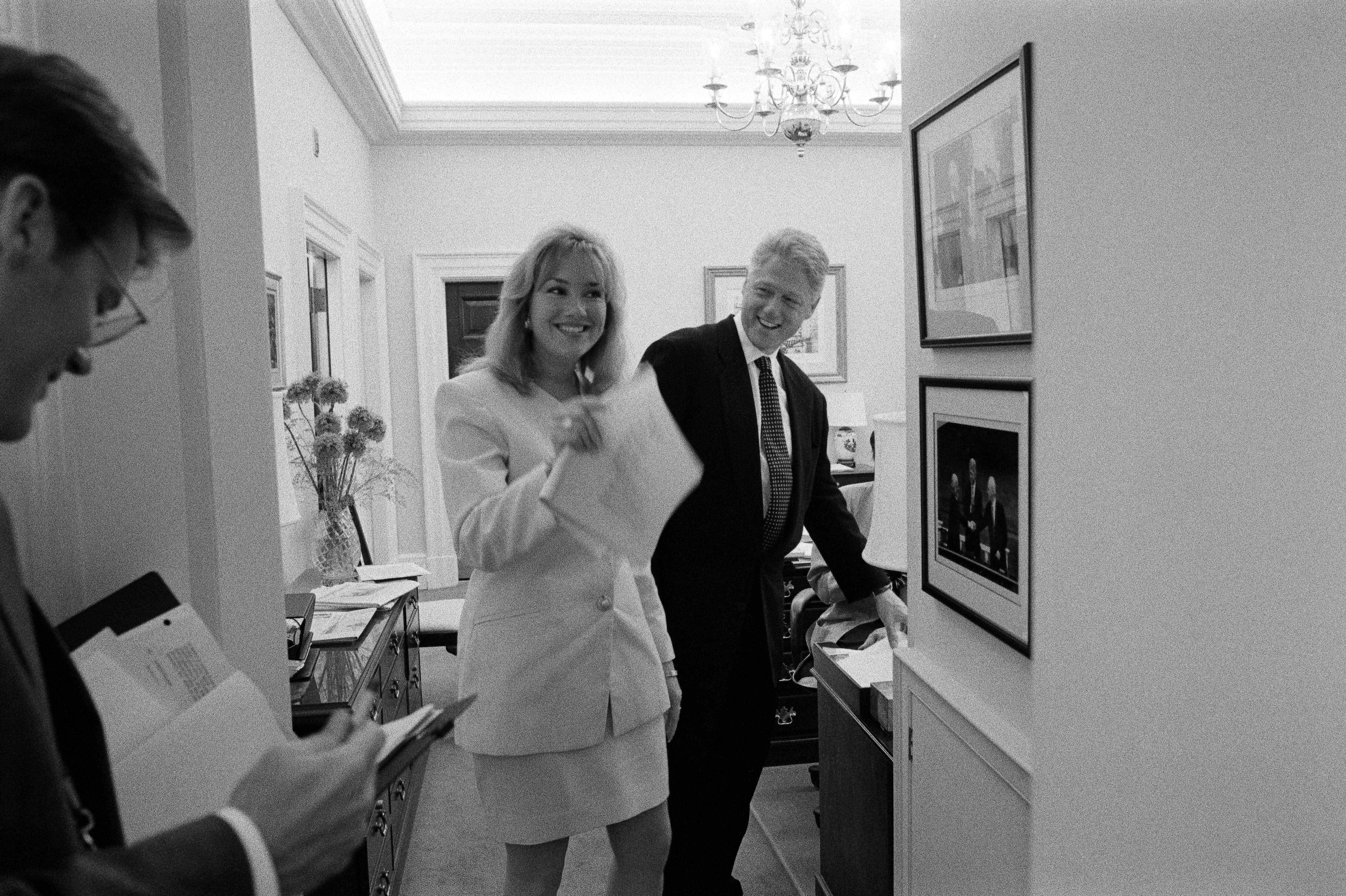 President Clinton laughs with Director of the Office of Scheduling and Advance, Stephanie Streett, and President's Aide, Stephen Goodin in the hallway outside of the White House Oval Office.  President Clinton, Street and Goodin all stand in the hallway. Goodin looks down at documents. 