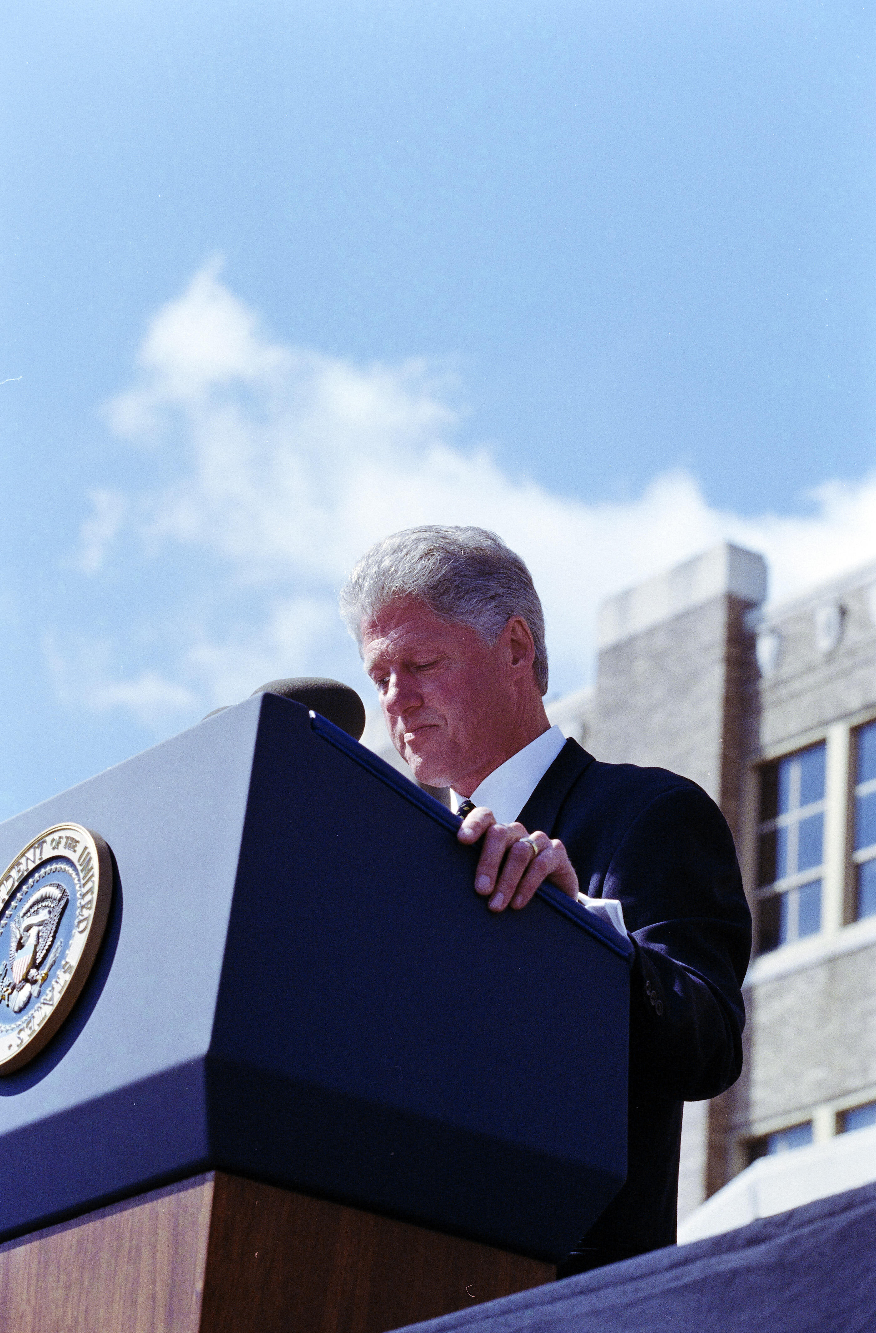 President Clinton stands behind a podium looking down at his speech.