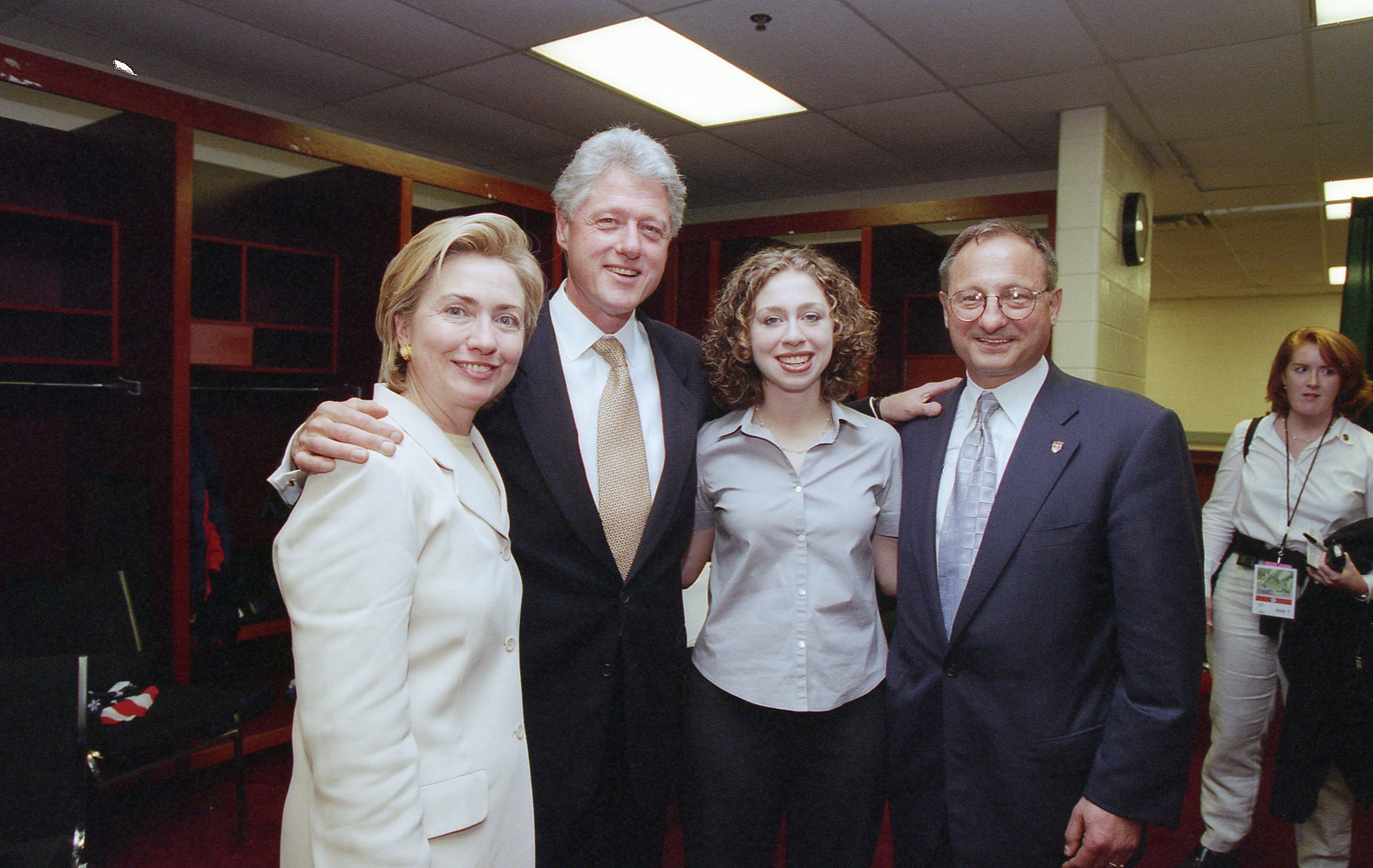 A photograph shows Hillary Clinton, Bill Clinton, Chelsea Clinton, and a man in a suit posing together inside what appears to be a stadium locker room.