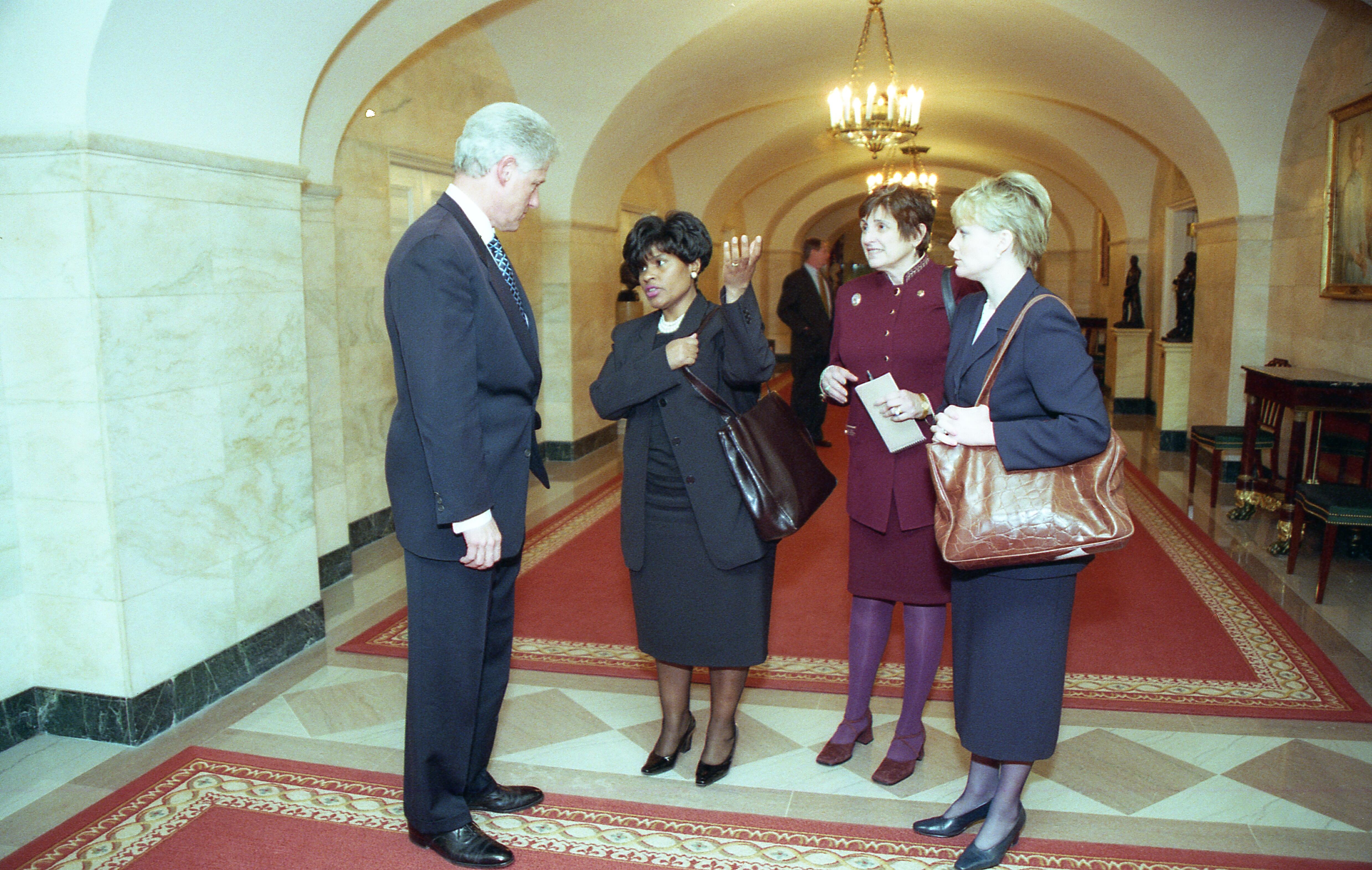 President Clinton stands and speaks with  Director of the Office of Public Liaison, Minyon Moore, Deputy Assistant to the President for Intergovernmental Affairs, Lynn Cutler, and Deputy Director of the Office of Political Affairs, Linda Moore in the hallway of the ground floor of the White House