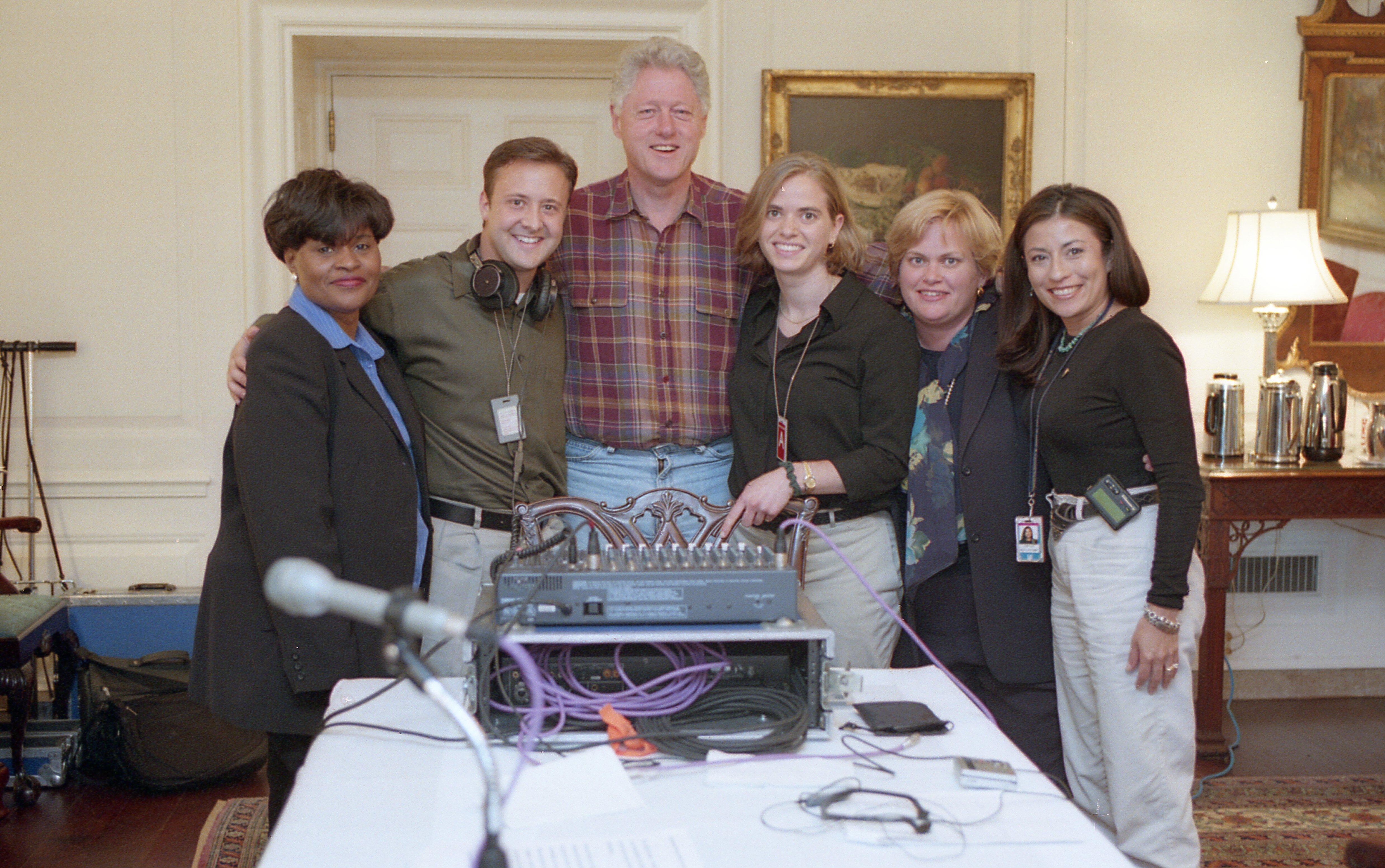 President Clinton stands in blue jeans. He poses for a picture with his arms around  Megan Maloney, Minyon Moore, and others.