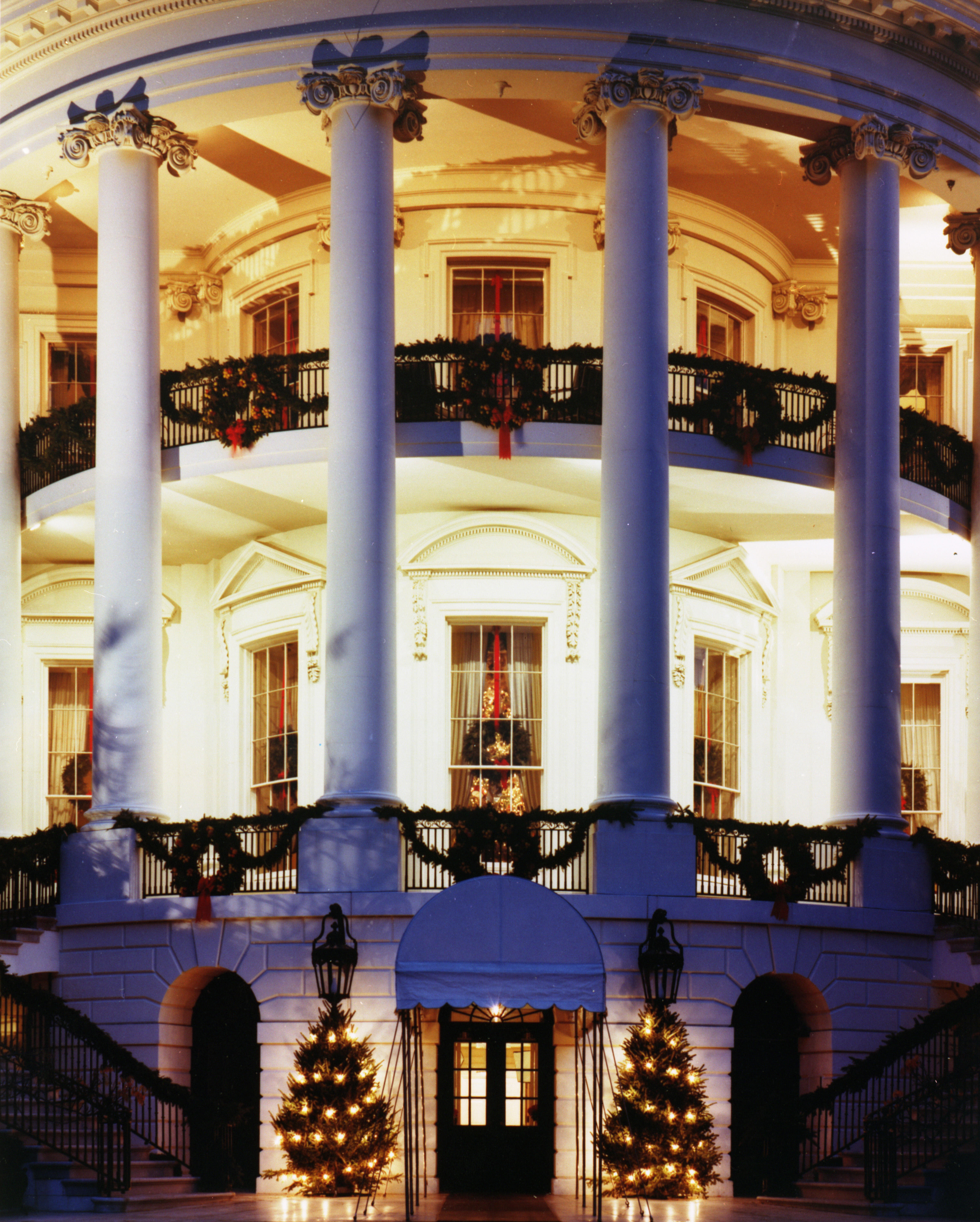 The South Portico of the White House decorated with garland, wreaths, and lighted trees.