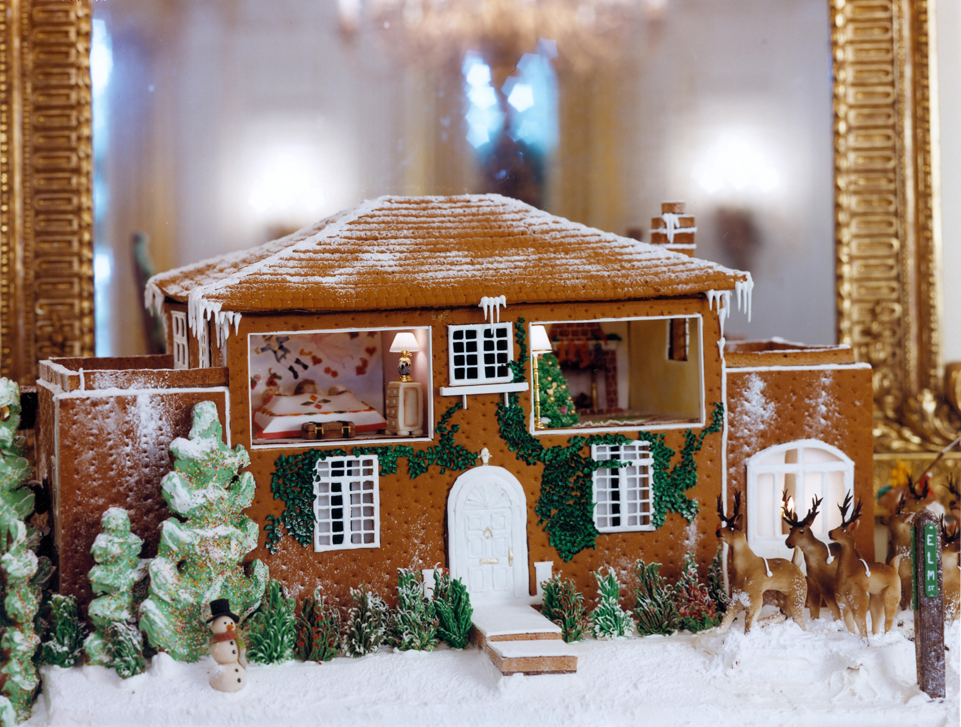 a two story brown gingerbread house with open windows on the second story so that you can view the inside of the house. 
