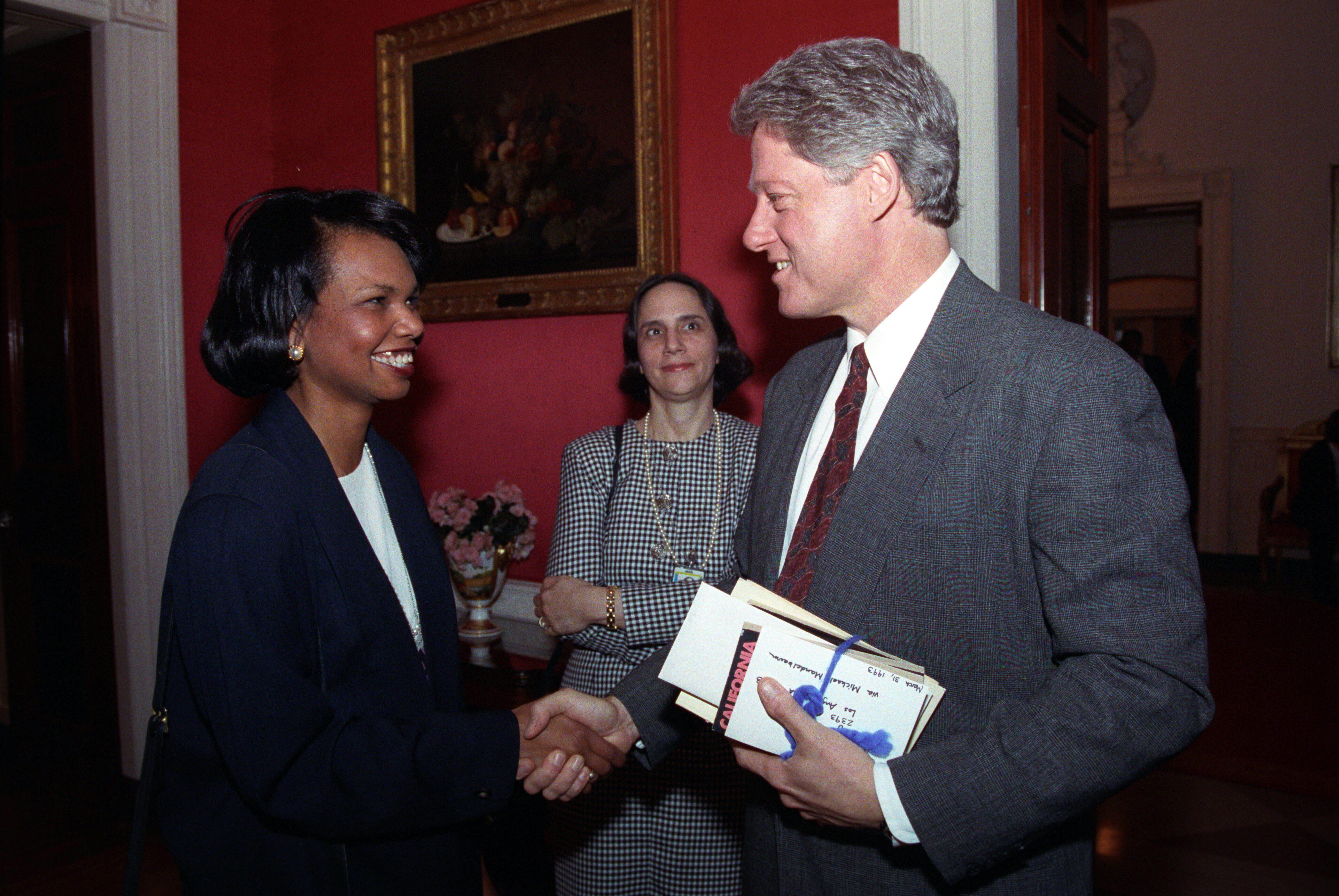 President Clinton shakes hands with Condoleezza "Condi" Rice. President Clinton holds a stack of correspondence in his left hand.