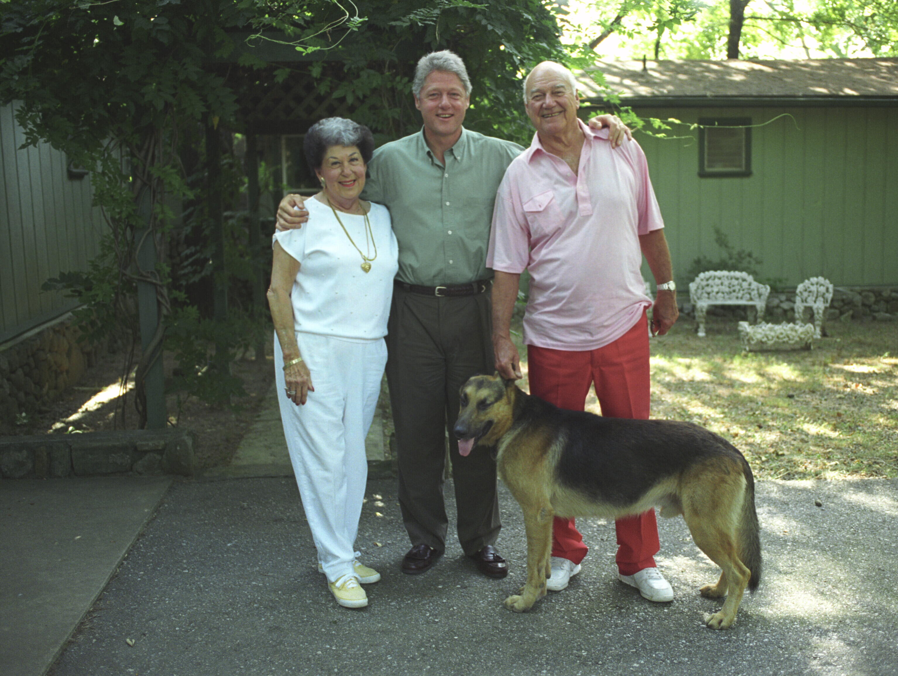 President Clinton poses for a photo with his mother, Virginia Kelly, step-father, Dick Kelly, and their dog, Champ, at their home in Hot Springs, Arkansas. President Clinton stands with his arms around his mother and step-father.