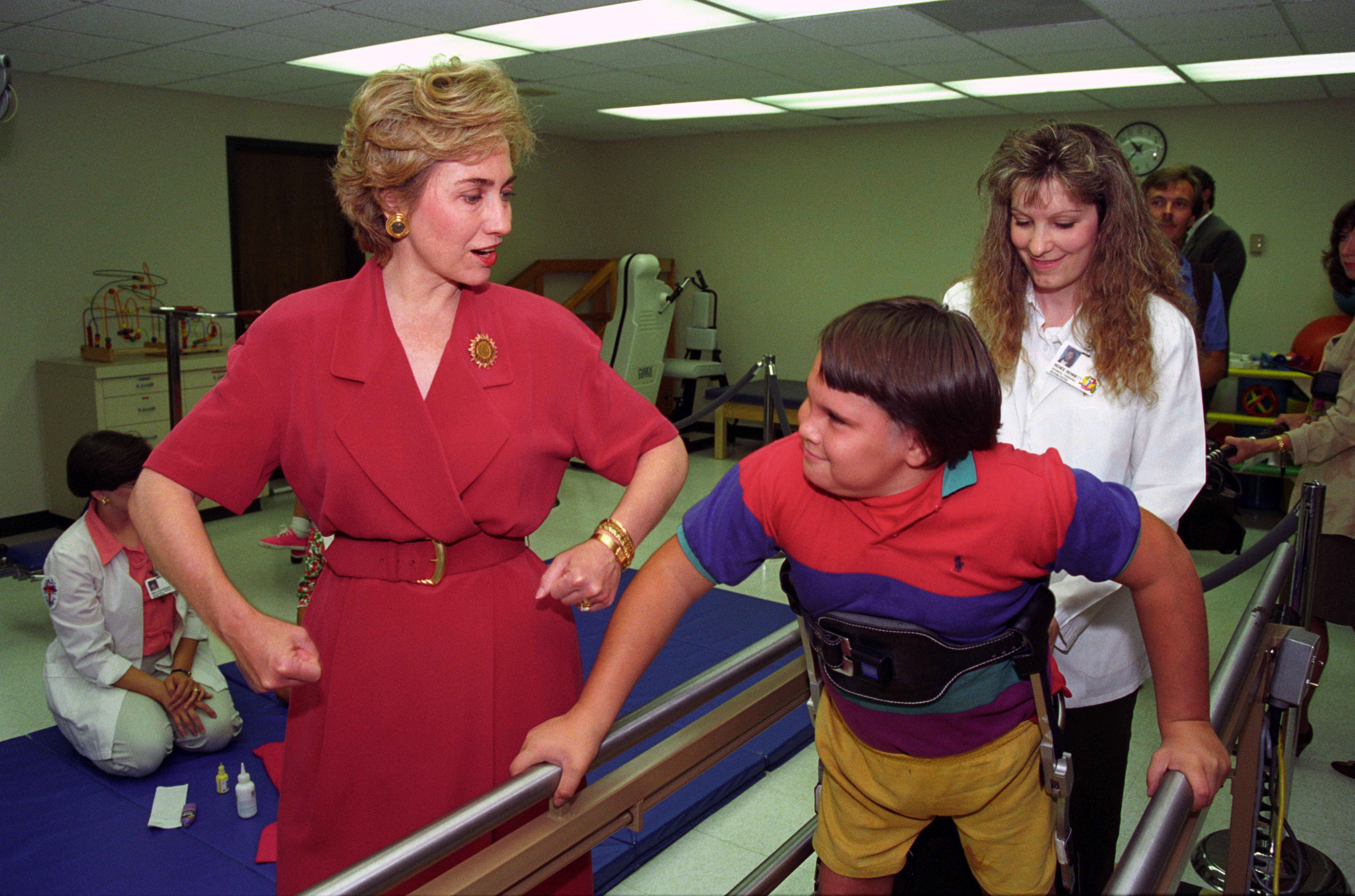 First Lady Hillary Rodham Clinton visiting the Arkansas Children's Hospital in Little Rock. The First Lady encourages a little boy in a physical therapy room while he is using parallel bars