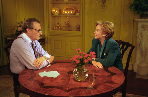 First Lady Hillary Rodham Clinton sits across from television personality, Larry King. They sit at a round table covered with a red table cloth
