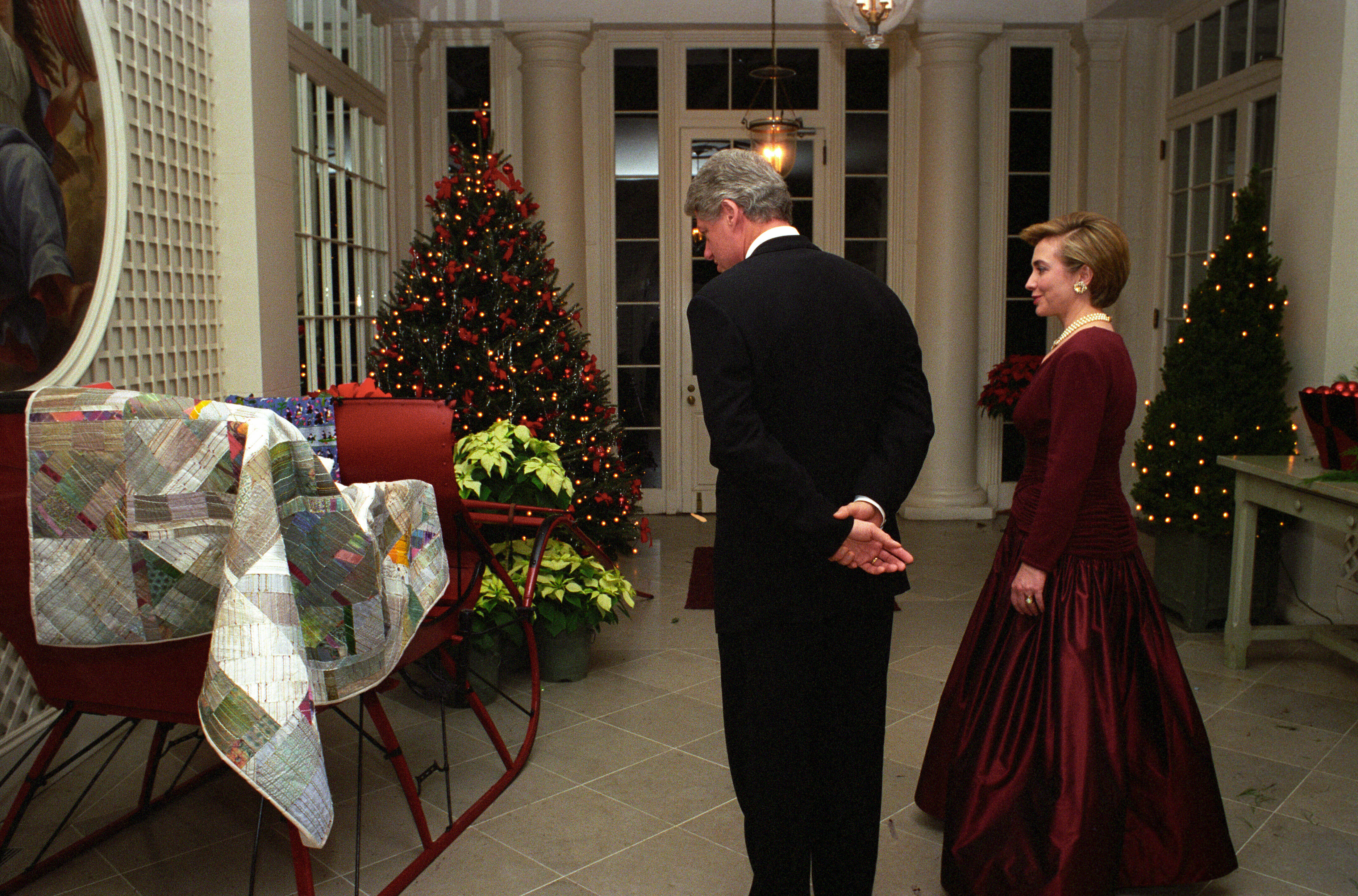 President Clinton and First Lady Hillary Rodham Clinton view Christmas decorations in the White House. In the photograph President Clinton and the First Lady look at a sleight with a quilt. They are dressed in formal attire