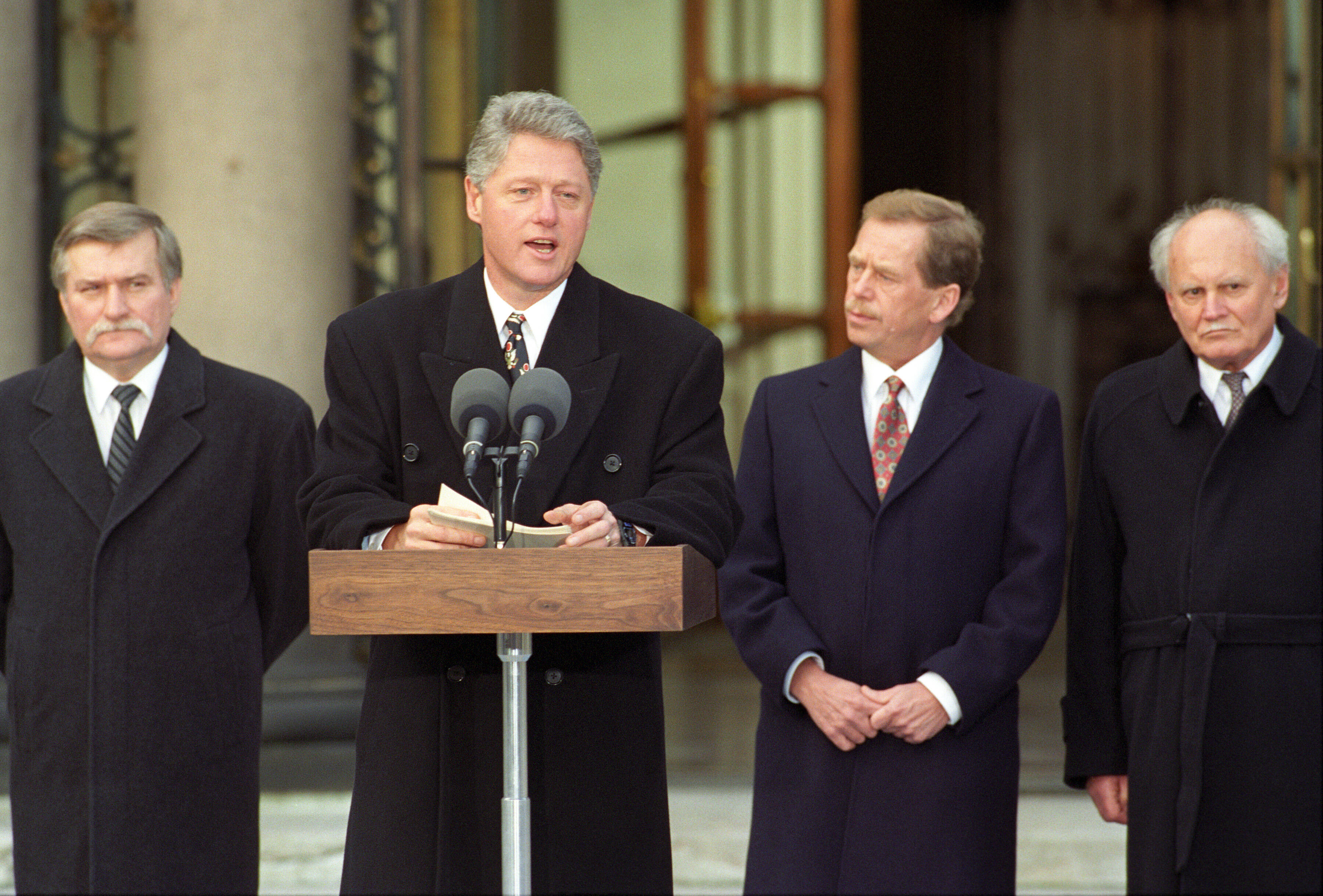 President Clinton stands behind a podium. President Lech Walesa of Poland, President Václav Havel of Czech Republic, and President Arpad Goncz of Hungary stand behind the President.