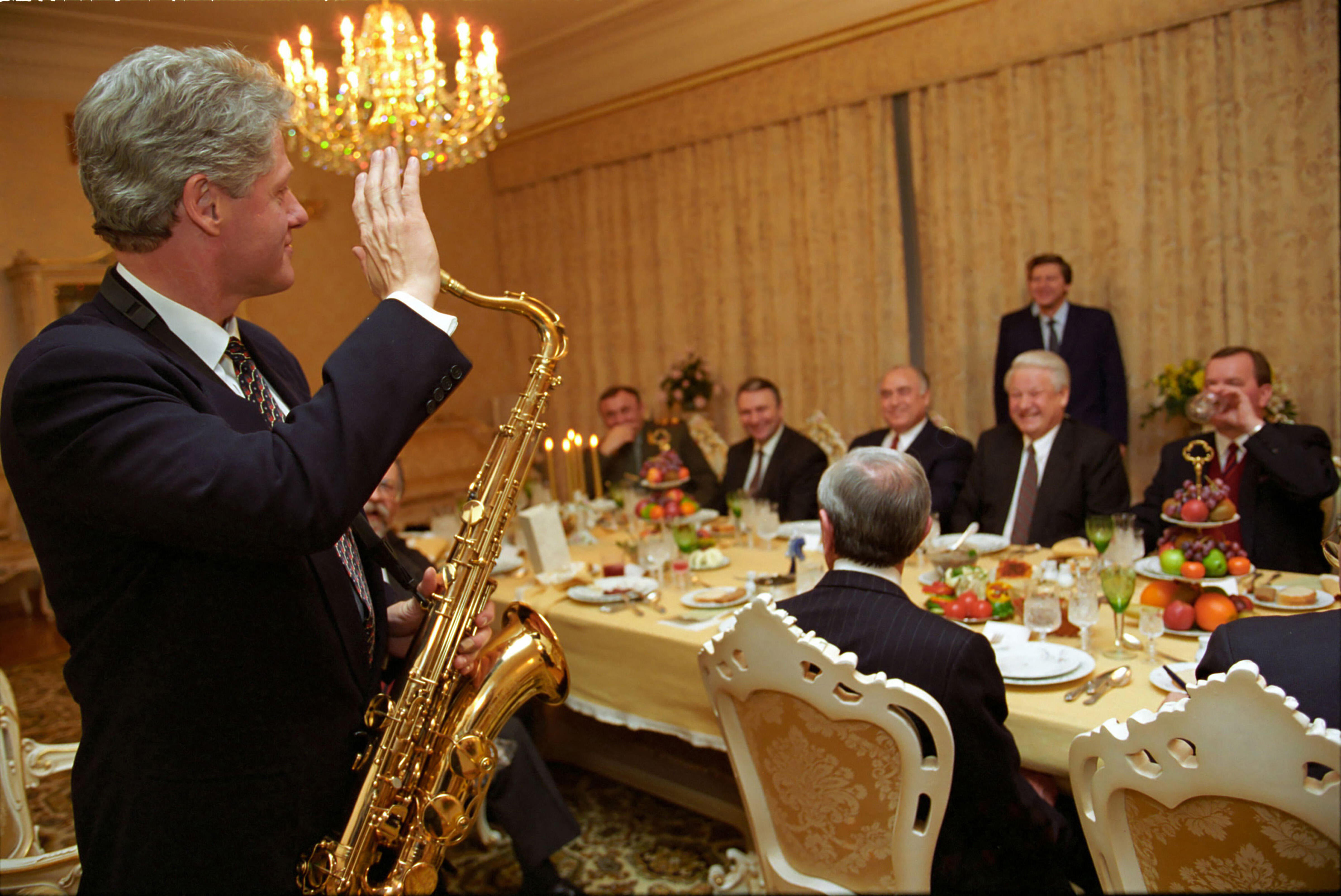 President Clinton plays a saxophone at dinner hosted by Russian President Boris Yeltsin at Novoya Ogaryova Dacha. Pictured at the dinner are President Boris Yeltsin, Secretary Warren Christopher, Secretary Lloyd Bentsen, National Security Advisor Tony Lake, Strobe Talbott, and Ambassador Thomas Pickering
