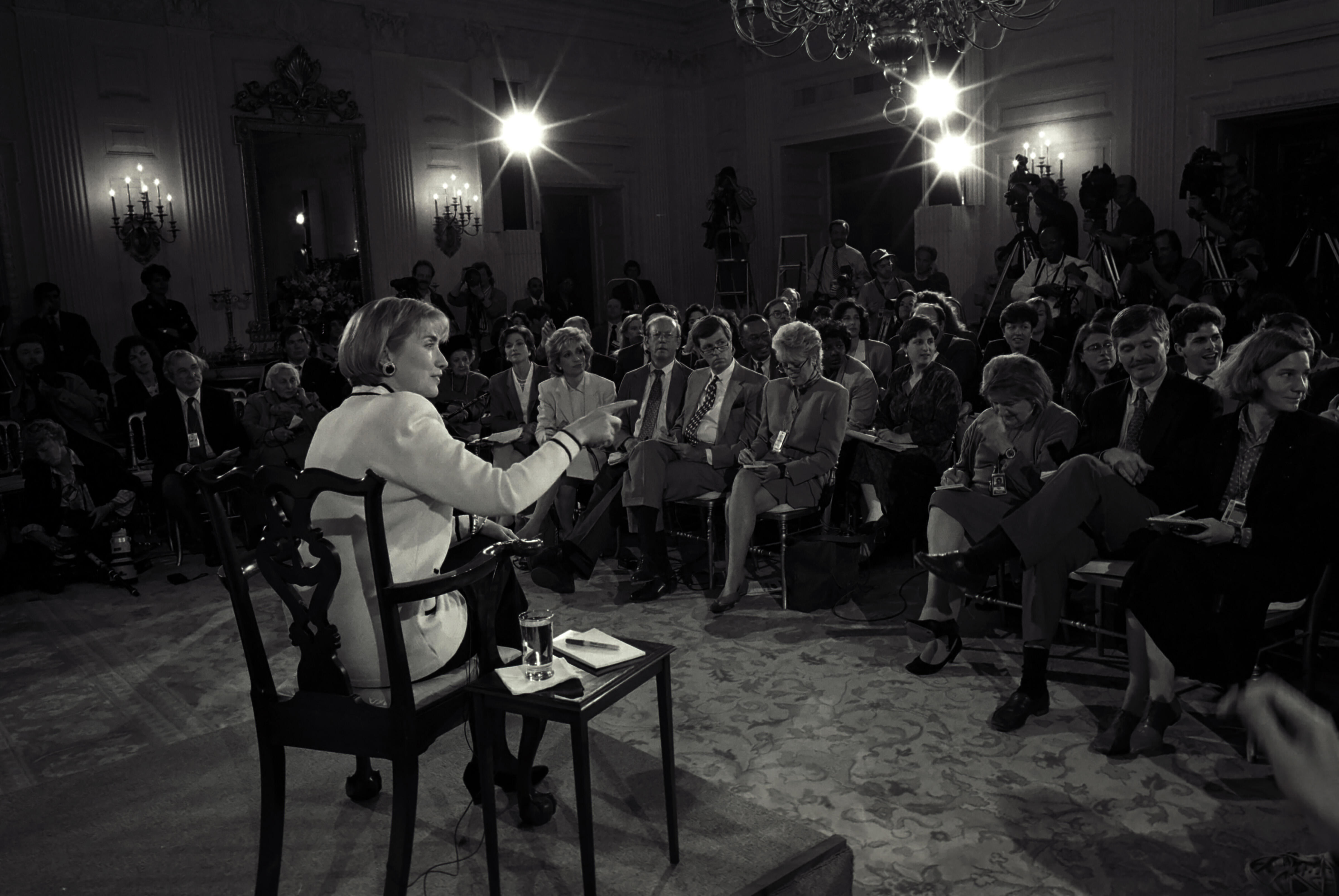 Black and white photograph. Hillary Rodham Clinton sits in the East Room of the White House and takes questions from the press concerning the Clinton's involvement with Whitewater and their financial investments