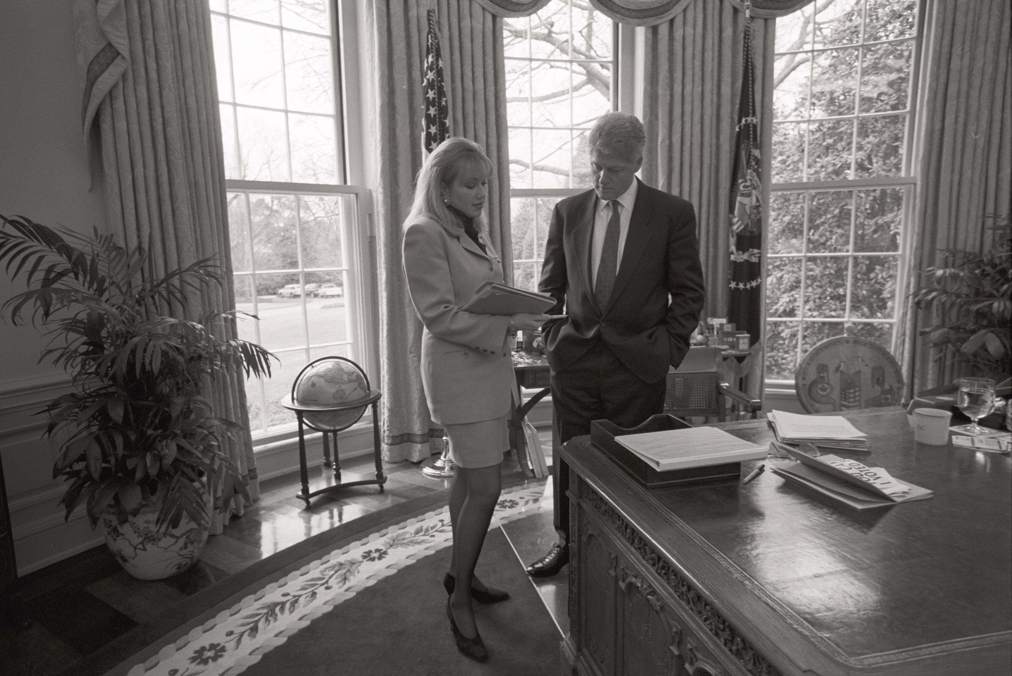 Black and white photograph. President Clinton meets with Stephanie Streett in the White House Oval Office. Both stand next to the windows in the Oval Office.