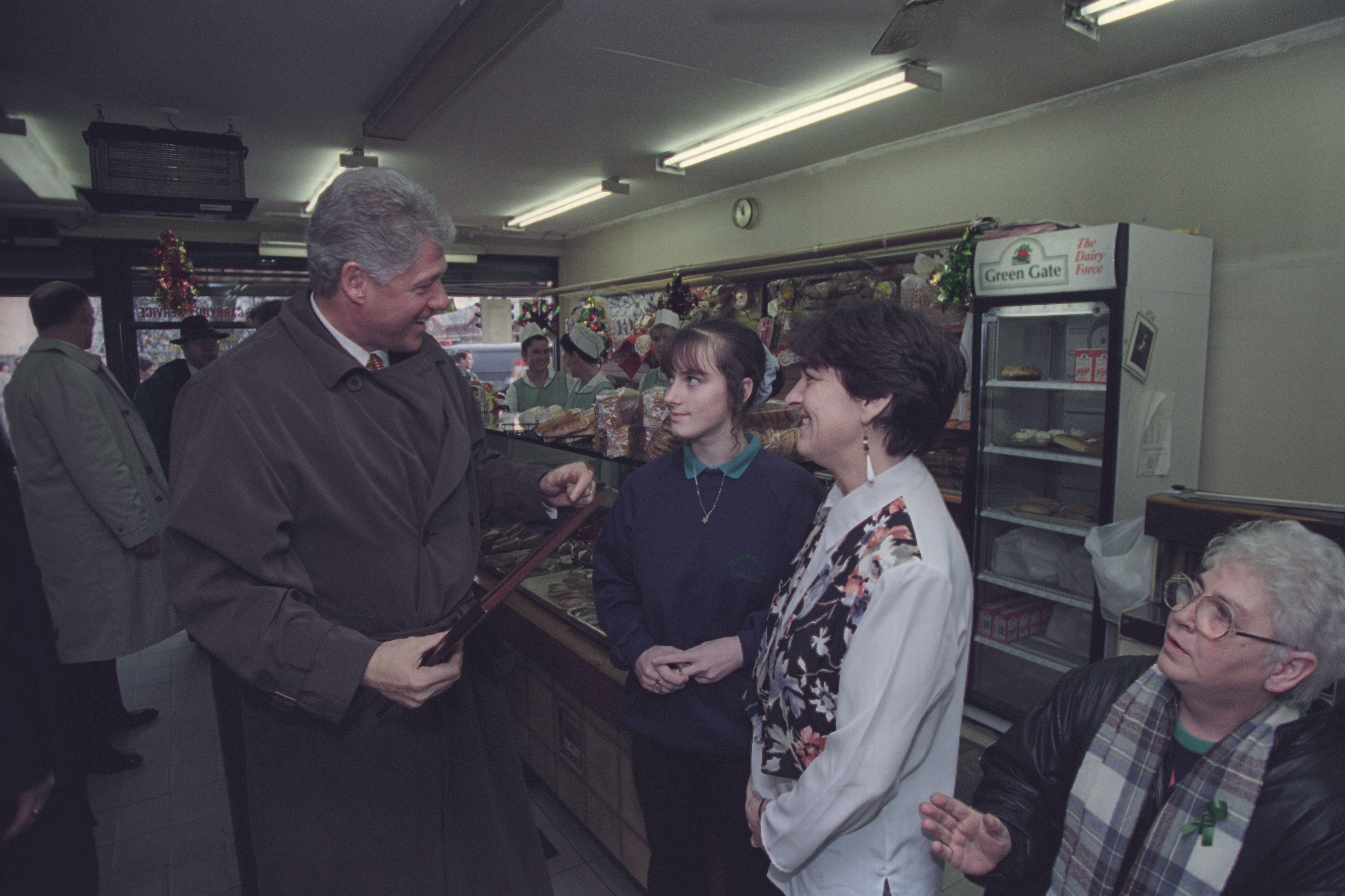 President Clinton talks to two women in a store. President Clinton and two women stand, and one woman sits, looking up.