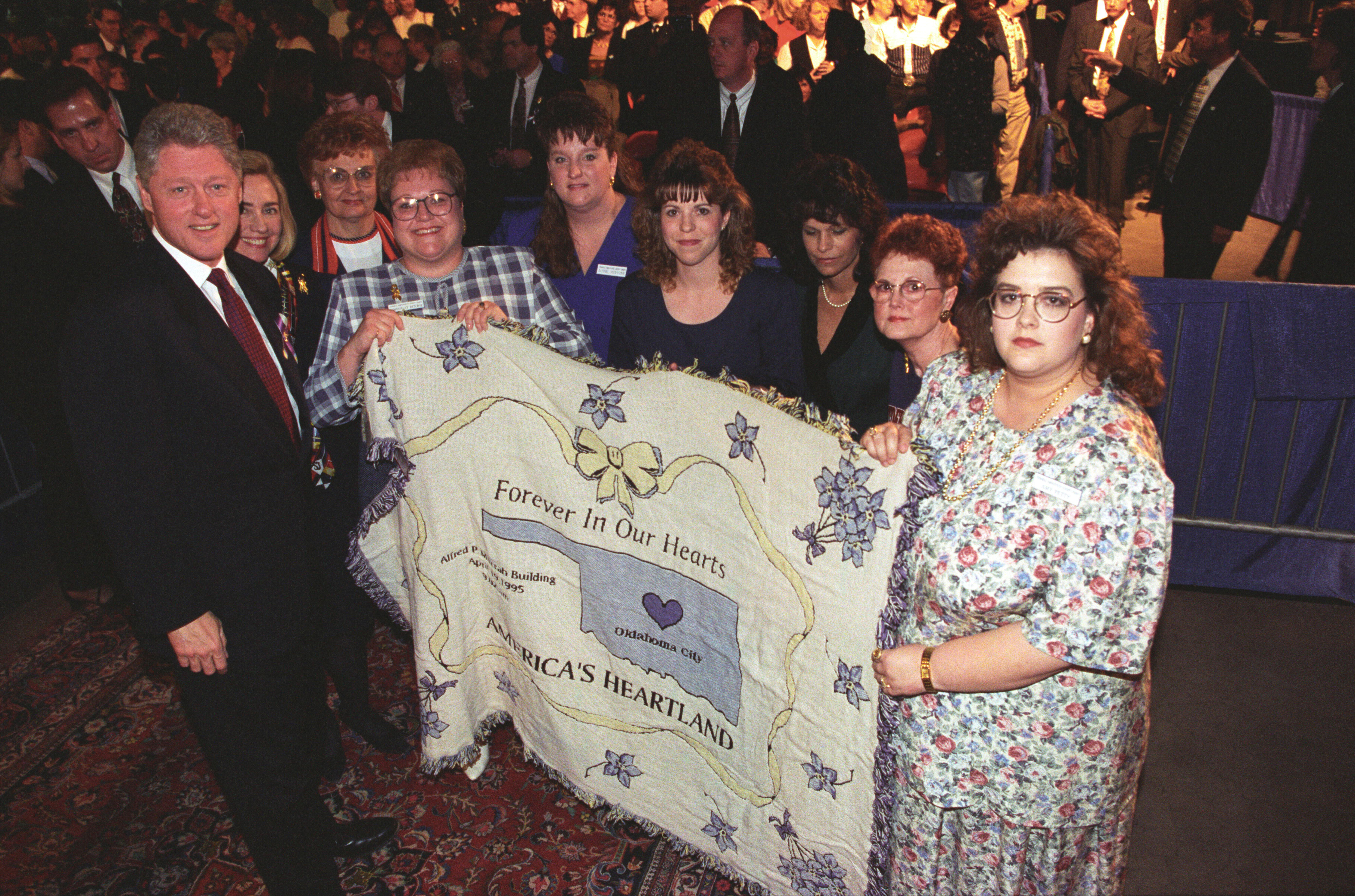 The Clintons are presented with a quilt that reads "Forever in Our Hearts Oklahoma City America's Heartland" during the anniversary memorial service for the victims of the bombing of the Murrah Federal Building in Oklahoma City. This event took place at the Myriad Convention Center.