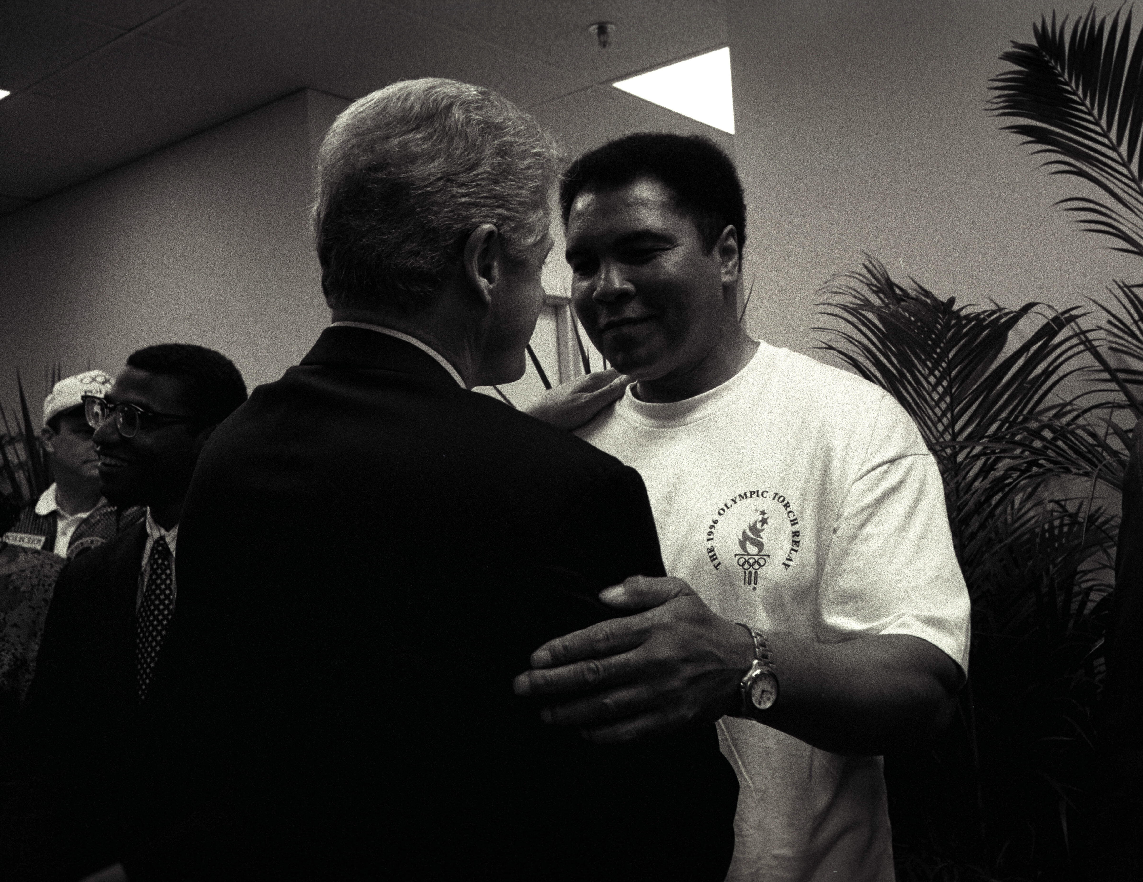 Black and white photo. President Clinton stands with his left hand on the shoulder of Muhammed Ali. Ali grips Clinton's rich arm with his left hand.