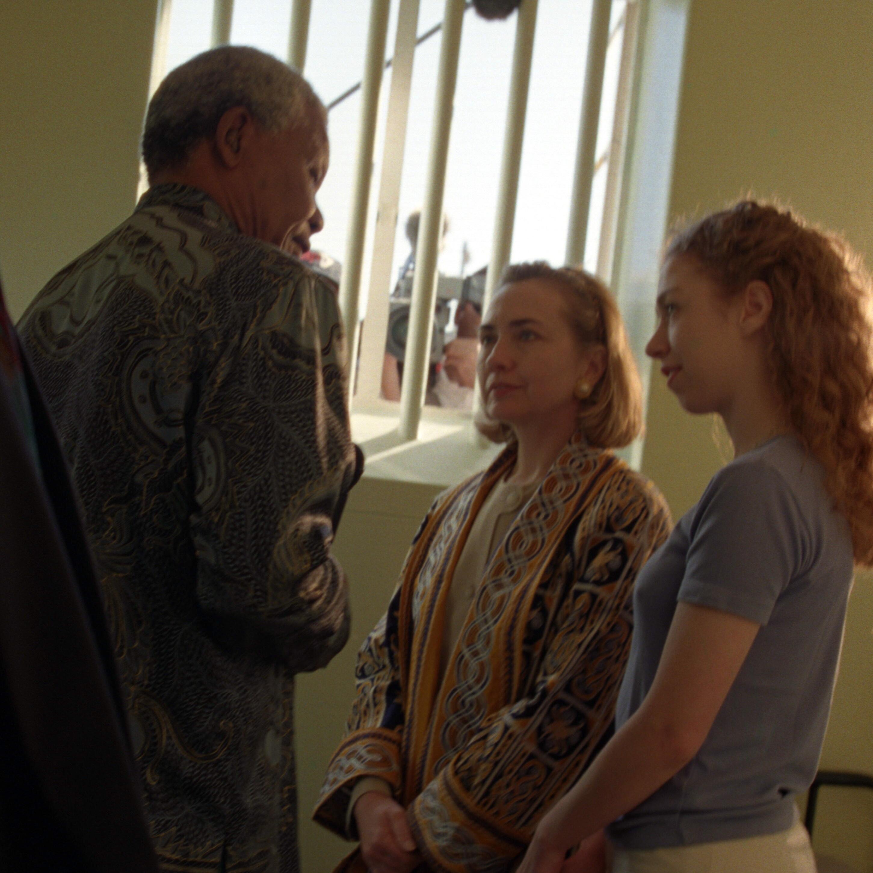 First Lady Hillary Rodham Clinton and daughter Chelsea Clinton stand while they listen to President Nelson Mandela. Prison bars are seen in the background.