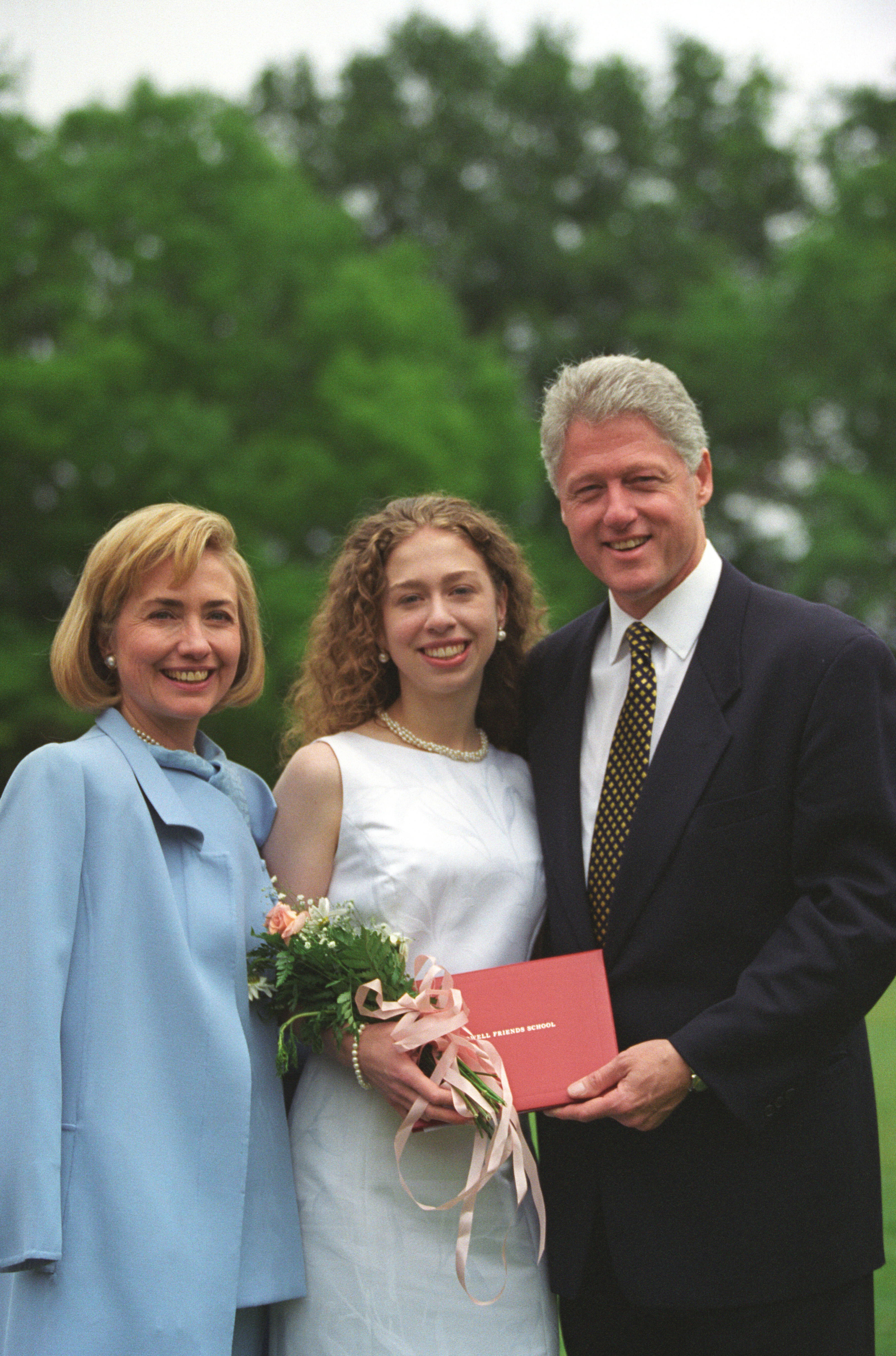 President Clinton, Hillary Rodham Clinton, and Chelsea Clinton pose for a photograph at Chelsea Clinton's high school graduation. President Clinton and Chelsea both hold Chelsea's diploma. Chelsea also holds a bouquet of flowers. 